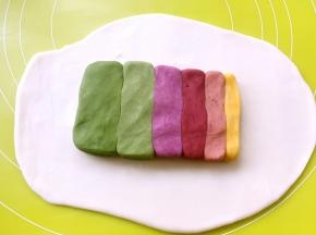 松弛好的水油皮面团擀成长方形，将6种颜色的油酥皮面团捏成同等长度，依次摆放在擀好的水油皮面团上
