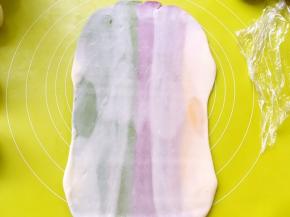 用擀面杖顺着彩色油酥皮纹路擀成长条，之后卷起来，盖保鲜膜松弛15分钟，擀的过程如果有气泡，可以用牙签扎破，再捏紧