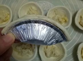 拿起一个挞皮对折，包住榴莲，边缘捏紧