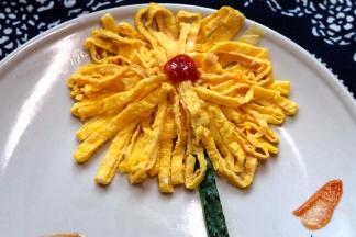 把切好的蛋皮摆在盘中，摆成一个菊花花朵的形状，中间挤上番茄酱当花心，再切点黄瓜条装饰一下，一朵漂亮的菊花就做好了。