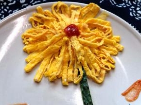 把切好的蛋皮摆在盘中，摆成一个菊花花朵的形状，中间挤上番茄酱当花心，再切点黄瓜条装饰一下，一朵漂亮的菊花就做好了。