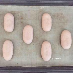 包好的面团捏紧收口，揉成长椭圆形的形状，放置烤盘中