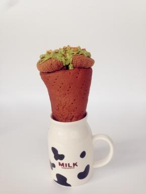 将面包桶放在高身杯中，将切成小粒的芒果放进面包桶底部，将蛋糕放上面。抹茶味巧克力隔水融化，淋在蛋糕上面，花生碎沾在巧克力上