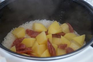 这时候米饭还剩20分钟，将土豆腊肠倒在饭面上，立即盖上锅盖