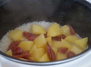 这时候米饭还剩20分钟，将土豆腊肠倒在饭面上，立即盖上锅盖