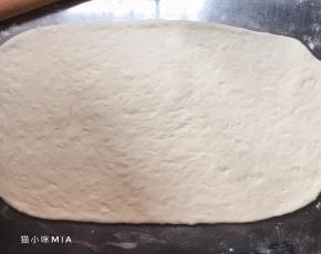 发好的面团排气，揉圆，用保鲜膜盖好，松弛10分钟，然后案板上撒干粉，将松弛好的面团擀成长方形状