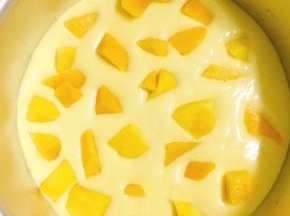 将拌好的慕斯馅倒入8寸蛋糕模具中，在中间撒上芒果肉