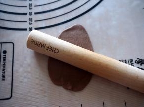 取一个可可小面团，擀成椭圆形面片，沿着长边卷起来，然后用手搓至比吐司盒稍微短一些。