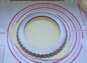 3、取出面团，排气；将面团擀开成较大的圆形面片，然后将披萨盘扣在面片上，用小刀去除多余的部分，盖上保鲜膜，静置15分钟二次发酵。