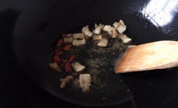 将猪肉的油炸出来后放红尖椒爆香，再将红尖椒挑出去，将大蒜去皮洗净整个放入锅中爆香