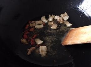 将猪肉的油炸出来后放红尖椒爆香，再将红尖椒挑出去，将大蒜去皮洗净整个放入锅中爆香