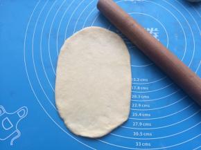 用擀面杖把面团擀成椭圆形状。