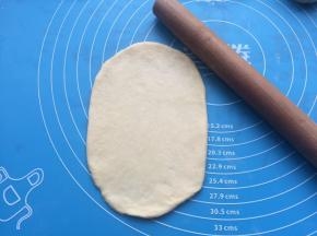 用擀面杖把面团擀成椭圆形状。