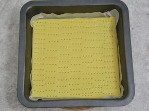 剪一张适合模具大小的油纸，取一半面团擀成油纸大小放入模具，用叉子叉出小洞，防止烤制时鼓起