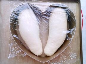 把阳晨碳钢8寸心形慕斯圈放在阳晨牛扎糖烤盘上把两个卷好的面团收口朝下放在模具里面盖保鲜膜进行二发。温度不要超过38度（50分钟左右）。