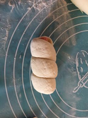 接着将长条柱面团的一端放至火腿肠一端上，将条柱形面团绕着火腿肠卷上（如图）