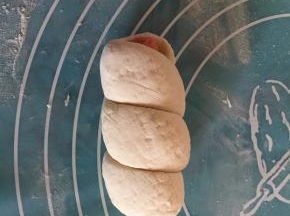 接着将长条柱面团的一端放至火腿肠一端上，将条柱形面团绕着火腿肠卷上（如图）