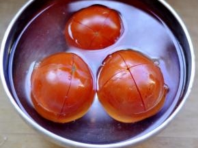2、开十字，放开水里泡5分钟后，剥皮。