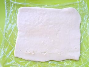 将保鲜膜上的原色面团，用擀面杖擀成0.2厘米厚的长方形