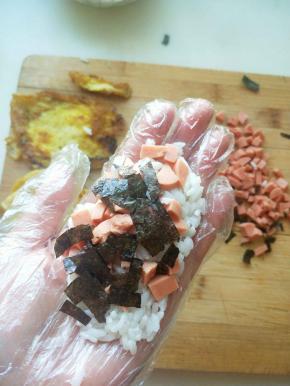 带上一次性手套先将米饭放在手心里，放上火腿肠和海苔，