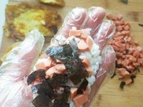 带上一次性手套先将米饭放在手心里，放上火腿肠和海苔，