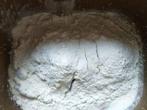 放入高筋面粉、全麦粉，最后挖个坑放入酵母。启动揉面程序20分钟。