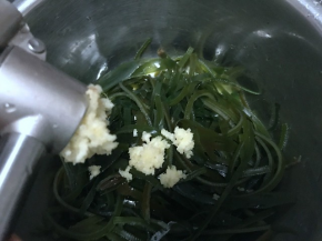把沥干水的海带丝放在小盆里，大蒜剥去外皮，用压蒜器压成蒜泥放进去；