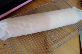 等蛋糕胚子温热以后，另取一张干净的烘焙油纸，将蛋糕卷起来，用油纸把蛋糕包好，使蛋糕卷形状固定；