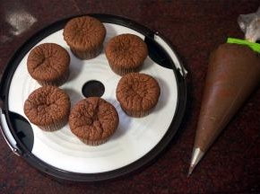 做好的巧克力奶油馅料装入带裱花嘴的裱花袋，将裱花嘴插入杯子蛋糕中，挤出馅料，蛋糕会重新变得饱满。