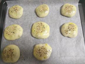 收口朝下放入烤盘，稍微压扁后刷上蛋液，撒上芝麻。