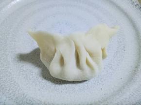 取一张饺子皮，盛一勺饺子馅放在饺子皮当中。将饺子皮对折起来，捏紧，捏出皱褶。