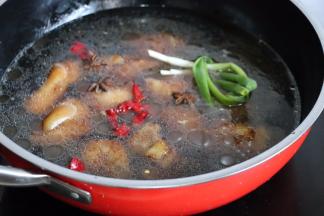 锅中加热水没过猪蹄，最好多加一点开水。葱打结，葱姜蒜、八角、辣椒一起放入