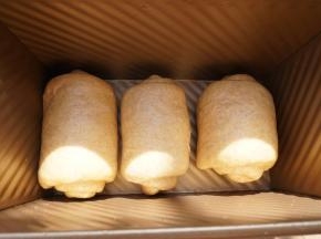 将其用手掌拍扁，再次擀开成牛舌状，边缘的气泡用手拍掉，上而下卷起，然后放入450克吐司盒排排站二次发酵