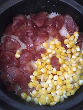 饭煮至八成熟的时候放入腊肠、玉米粒，盖上盖子用小火焖煮十分钟关火，先不揭盖继续焖十五分钟