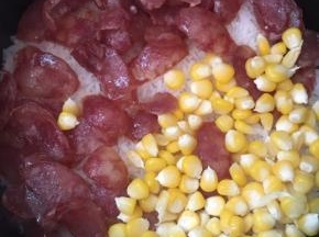 饭煮至八成熟的时候放入腊肠、玉米粒，盖上盖子用小火焖煮十分钟关火，先不揭盖继续焖十五分钟