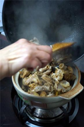 将炒锅里的羊肉转移到砂锅上焖煮。