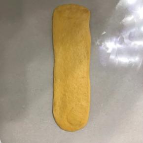 取一个长面团用手掌拍扁排气，再用擀面杖从中间向二头擀成长舌型，尽量保持一样宽，边上的气泡用手拍掉。