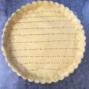 冰箱里冷藏的面团拿出来，擀成0.5厘米左右的圆片，放进派的模具里，我这个模具是8寸的，用叉子叉一些孔，以免派皮受热膨胀鼓起来