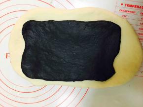 将原色面团与竹炭面团擀成长方形，将竹炭面团覆盖到原色面团上，四周留一些原色