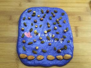 1大份的蓝色面团也擀成长方形，最下方摆一排大杏仁，上面撒上葡萄干和榛子仁。