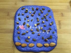 1大份的蓝色面团也擀成长方形，最下方摆一排大杏仁，上面撒上葡萄干和榛子仁。