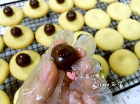 取一颗麦丽素挤上少量巧克力酱，粘贴在曲奇饼干中间的凹洞中。