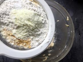 然后将面粉、南瓜粉、奶粉一起筛入黄油鸡蛋糊中。