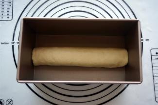 然后从一边讲面片卷起，收口朝下，放入吐司盒中。另一个面团也是同样的操作。将两个吐司盒盖上保鲜膜，放入烤箱进行二次发酵，温度35度。