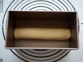 然后从一边讲面片卷起，收口朝下，放入吐司盒中。另一个面团也是同样的操作。将两个吐司盒盖上保鲜膜，放入烤箱进行二次发酵，温度35度。