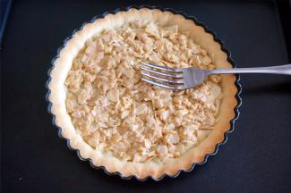 将杏仁焦糖牛轧糖趁热铺到派塔上，用叉子背摊平。