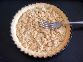 将杏仁焦糖牛轧糖趁热铺到派塔上，用叉子背摊平。