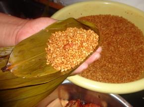 把粽叶折叠成漏斗形状。 在这个漏斗中先放一小把米，再放入五花肉和蛋黄，然后再放点米把肉盖住。米和漏斗口持平即可，太少了粽子很瘪，太多了包不住。