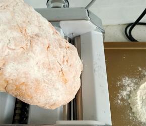 将面团用手按扁，启动压面机