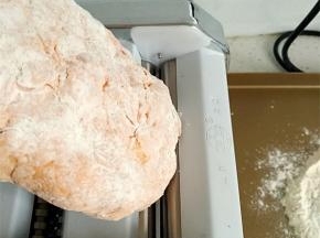 将面团用手按扁，启动压面机